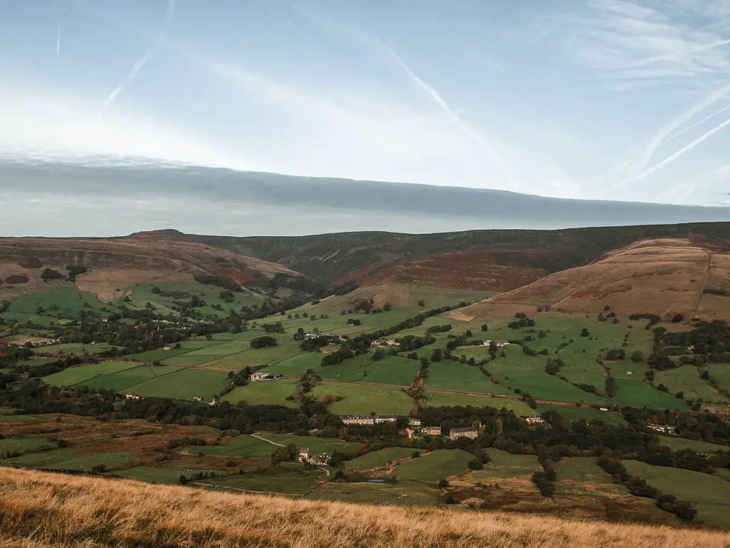 Looking down into the valley filled with fields lines with trees, and some hills on the other side in the Peak District National Park.