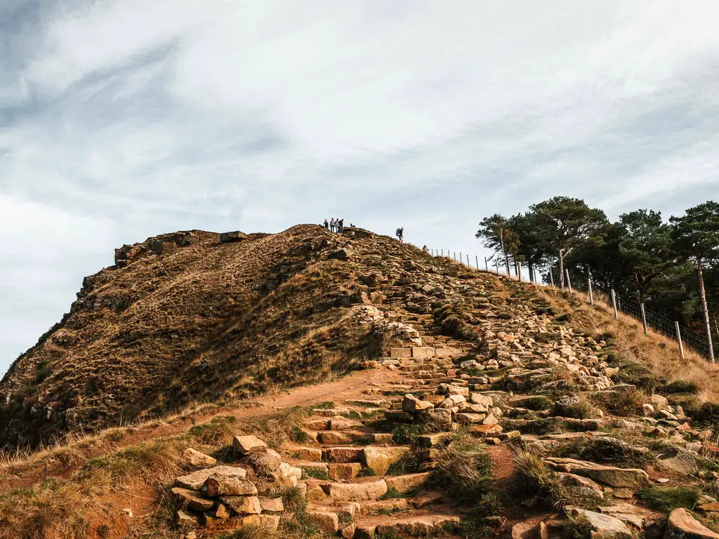 A rugged stone path and steps leading up Back Tor. There are a few people standing on the top.