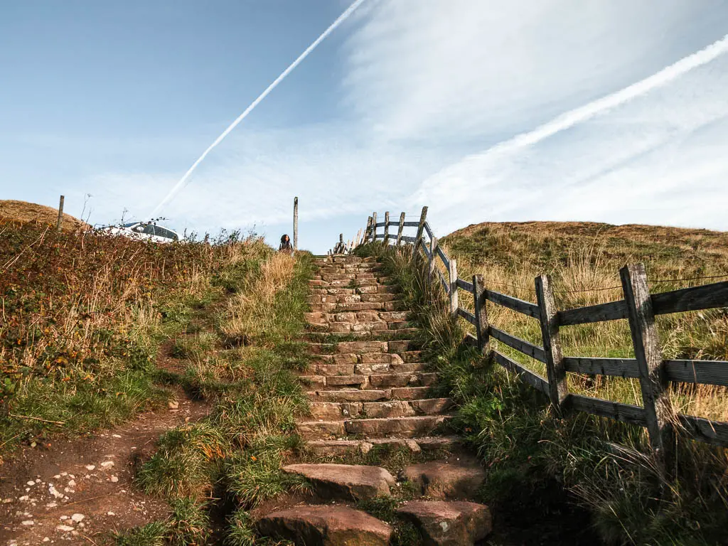 Stone steps leading up, with grass and dirt to the left and a wooden fence to the right.
