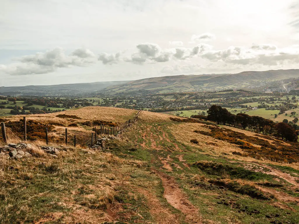 Dirt trail leading downhill, with a wooden and wire fence on the left.