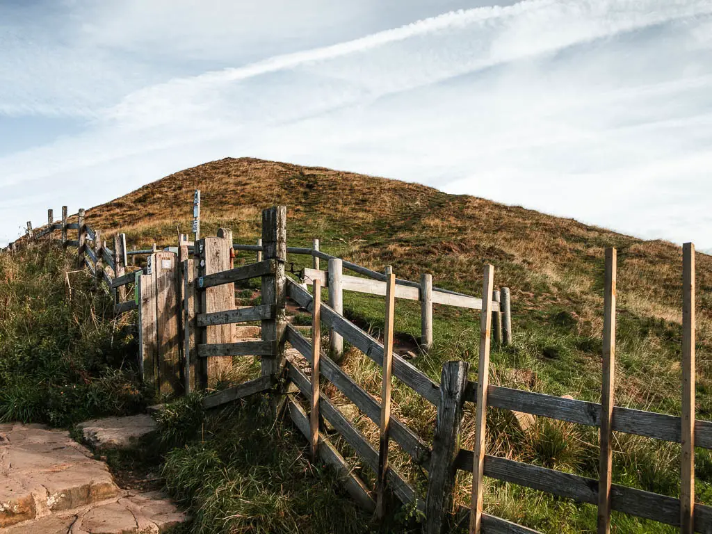 A wooden fence with a hill on the other side.