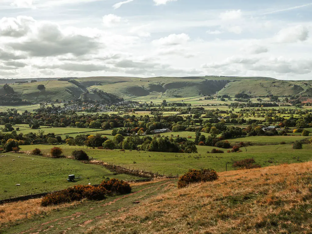 Looking downhill into the valley of grass fields lines with trees, and hills in the distance on the other side.