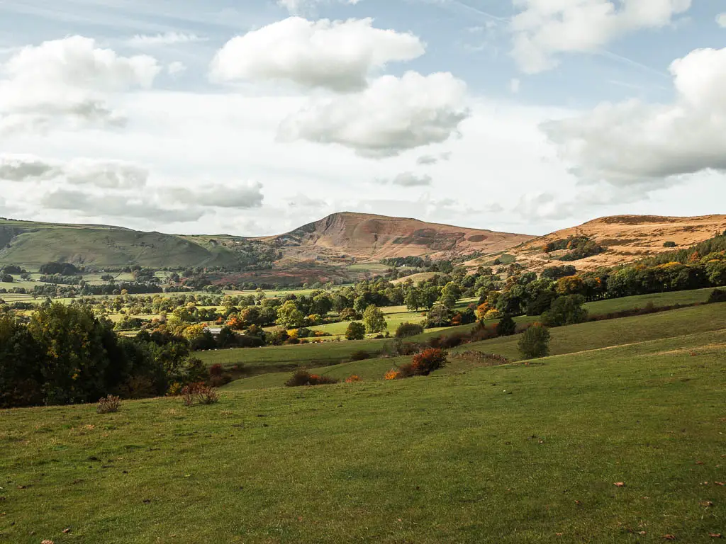 A big field leading to fields with trees and Mam Tor in the distance, part way through the circular walk.