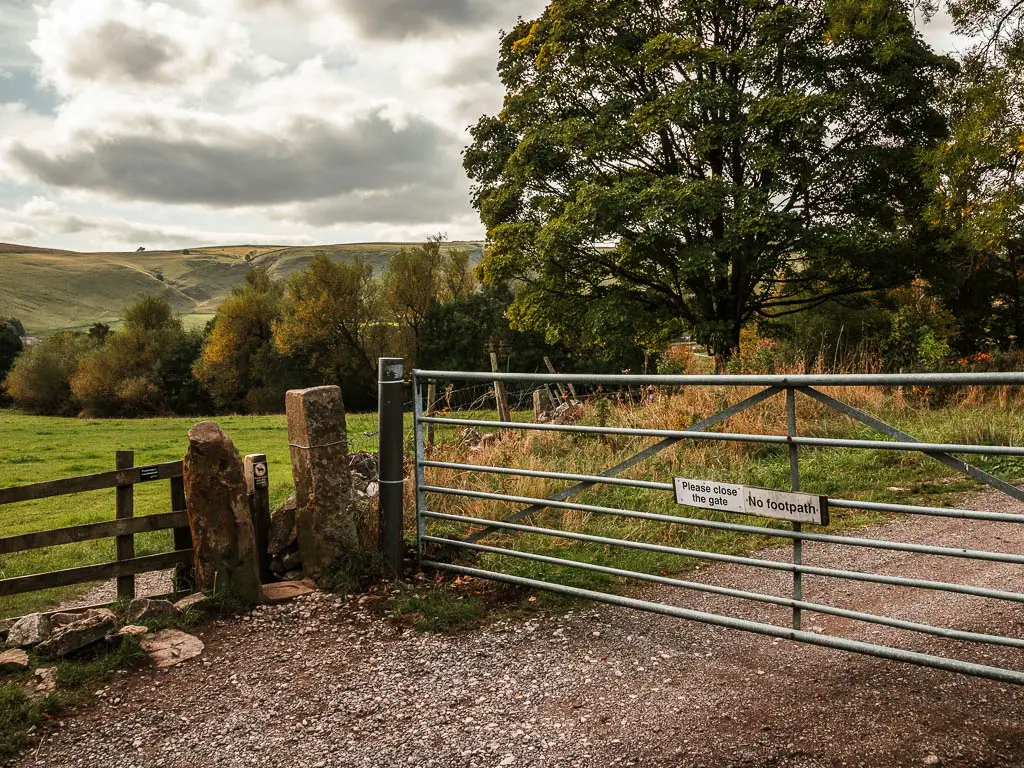 A metal gate with a sign saying 'no footpath', and a small wooden gate to the left of it.