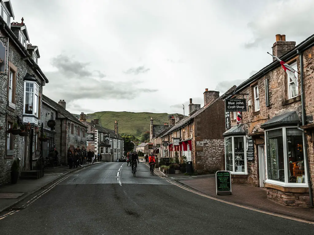 Looking down the road lines with shops and houses in Castleton. There are a couple of cyclists on the road.