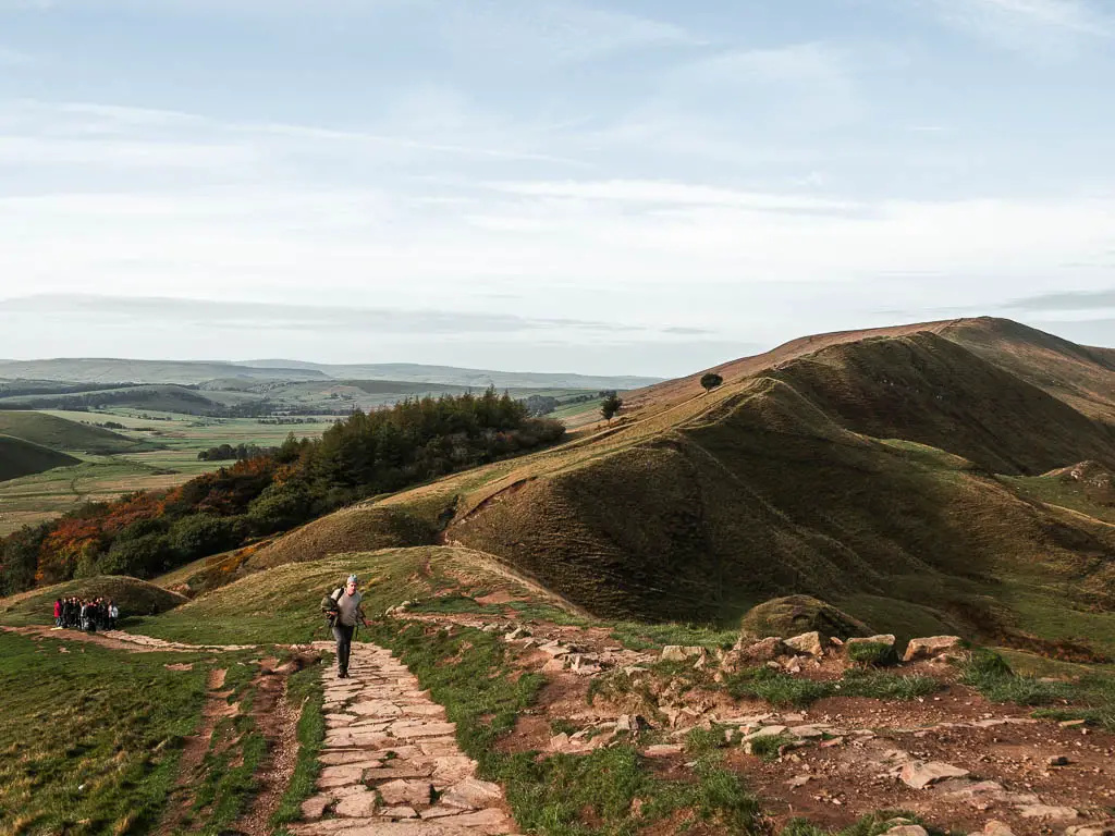 Looking down the stone paved path towards a ridgeway. There is a man walking on the path.