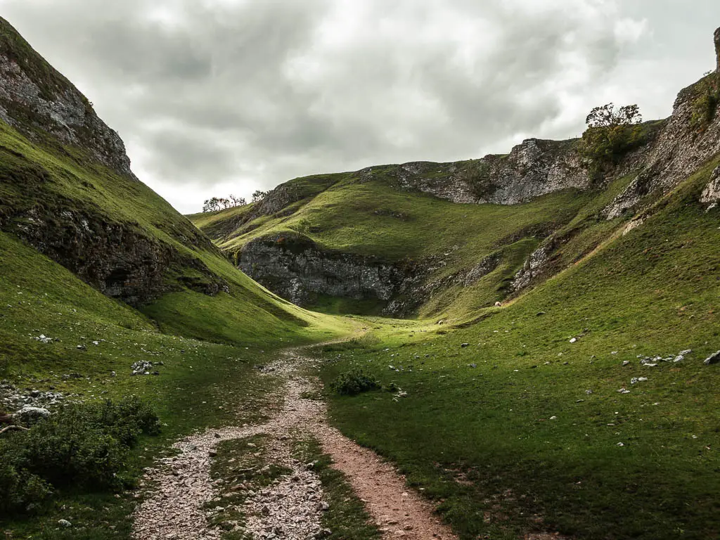 A stoney path through the valley of Cave Dale. The hills are covered in short green grass, with rocks at the top of the hills.