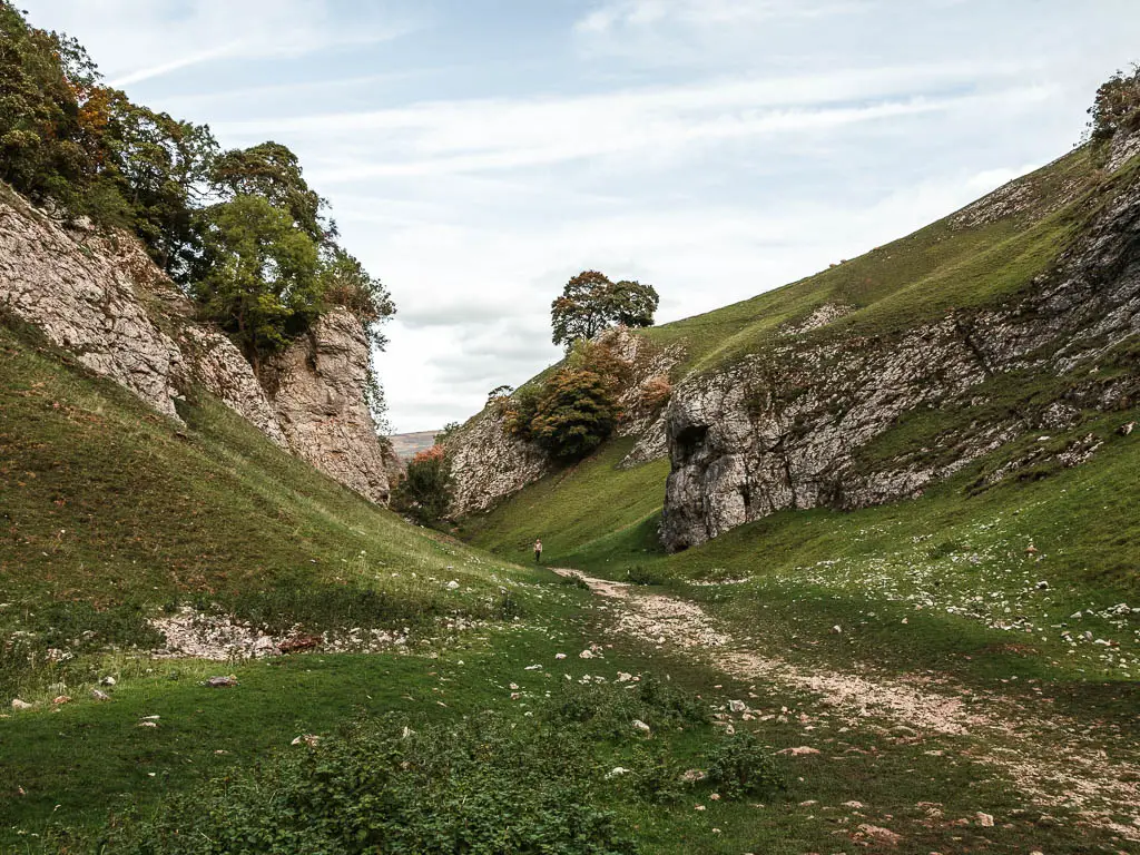 Looking through the valley of Cave Dale, with a slither rocky path, green grass hills on other side, and rock ledges justing out from the hill sides.