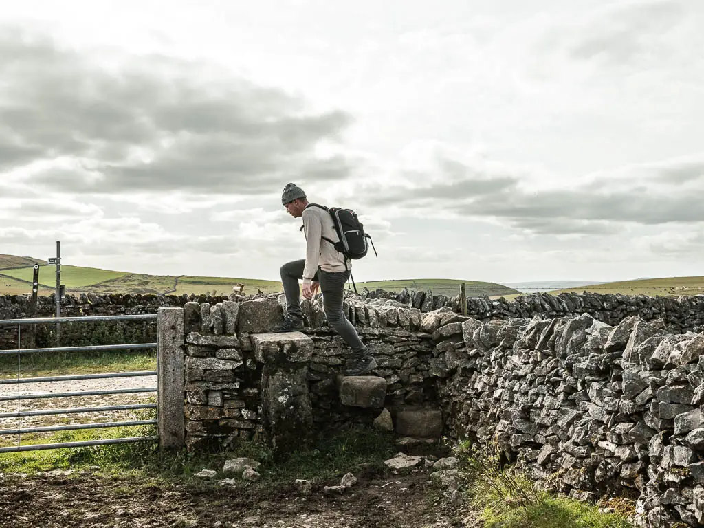 A man walking up stone steps over the stone wall, on the walk back to Mam Tor.
