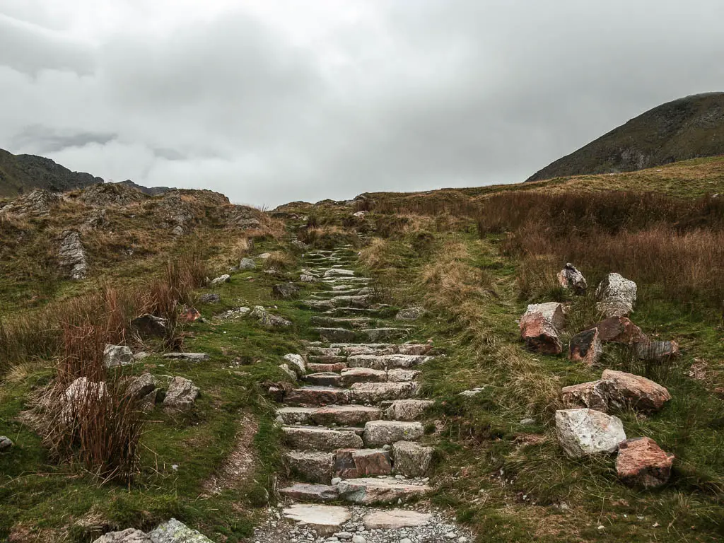 Stone steps leading uphill, surround by grass, on the walk route to the Old Man of Coniston.