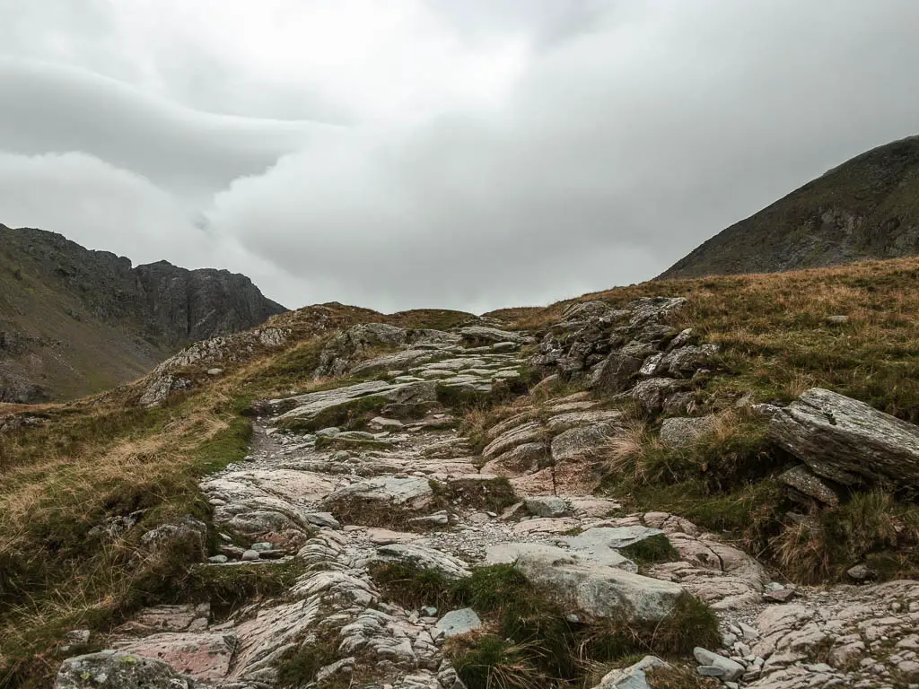 A rugged rocky path leading up, surrounded by grass.