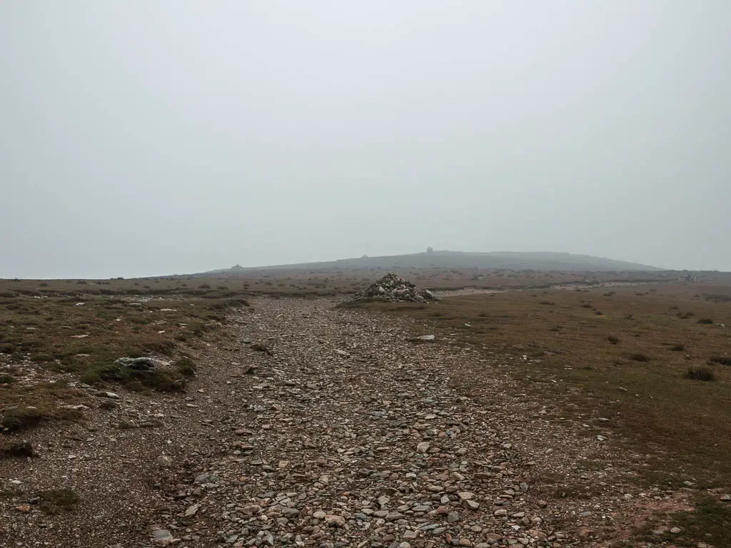 A wide rocky path surround by short grass, with mist everywhere.