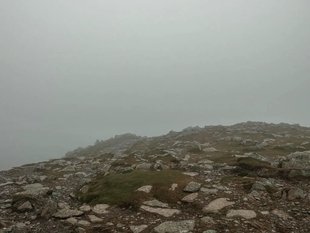 A ground of rocks and grass with no visibility ahead due to the fog and mist.