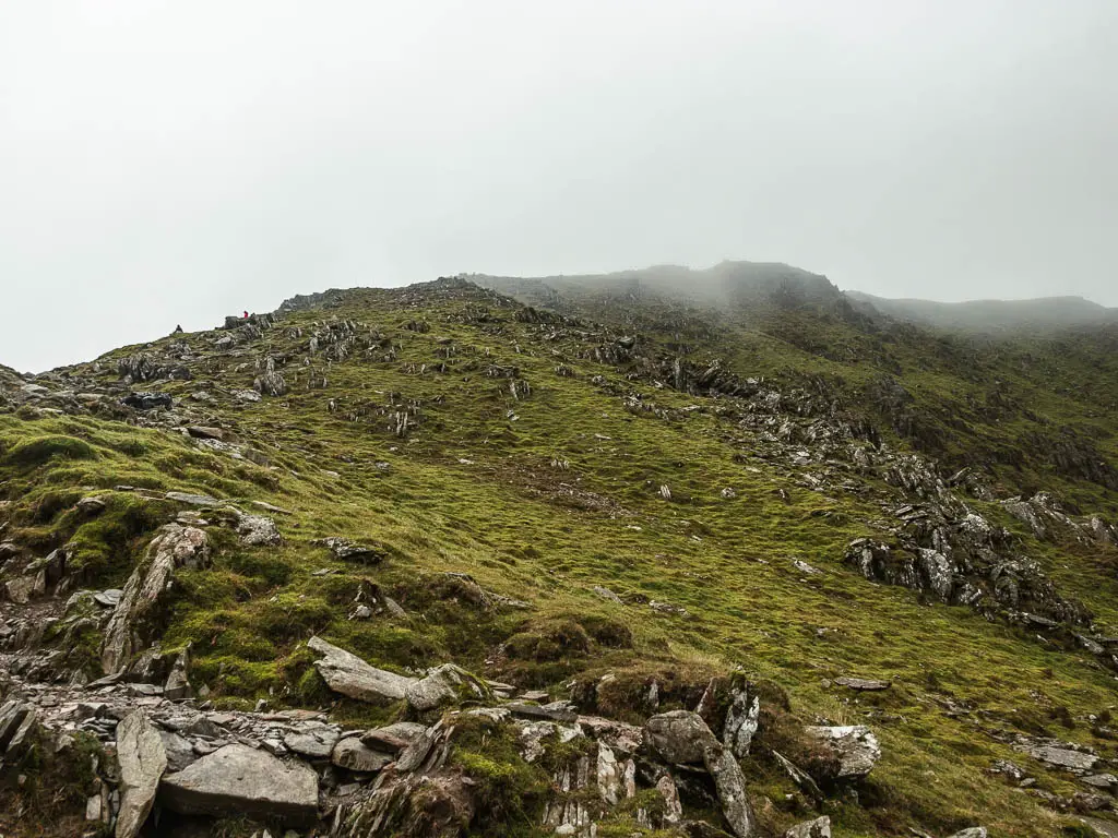 Looking up the grass and rock covered hill, with mist higher up.