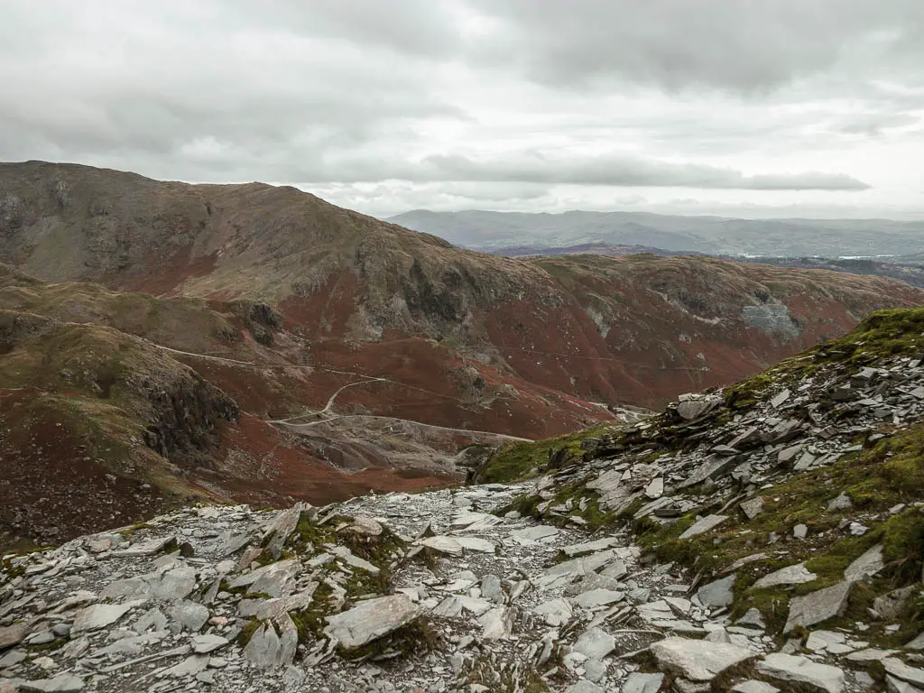 A trail of slate rock leading downhill, with a rugged fell ahead in the distance. 