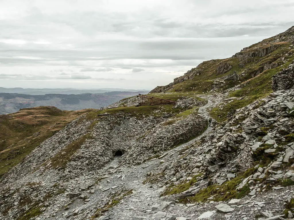 A path surround by grey slate rock and a fallen pylon ahead on the walk route down off the old man of coniston.