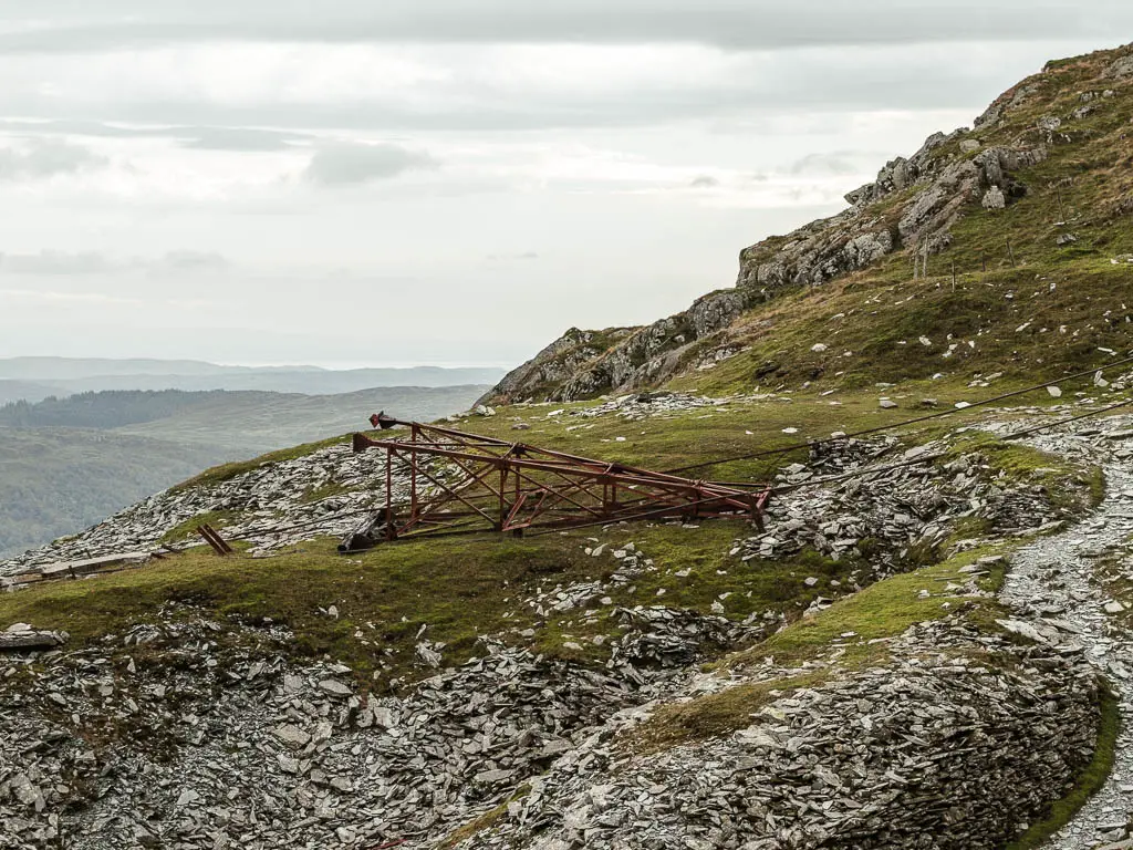 A fallen pylon on the grass, surround by slate rock on the walk route down off the Old Man of Coniston.