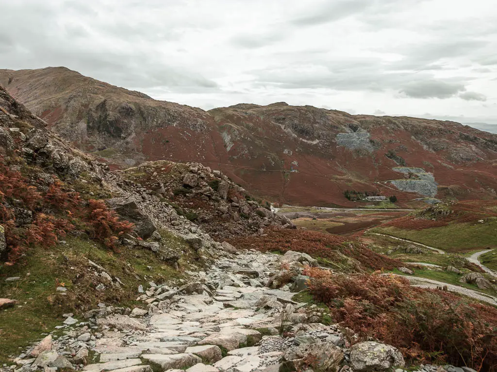 A rocky path leading downhill with fells rising ahead. 