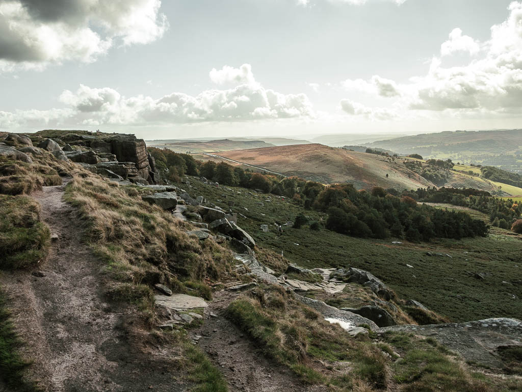 A dirt rocky path on the walk down off Stanage Edge, with the woodland plantation ahead.