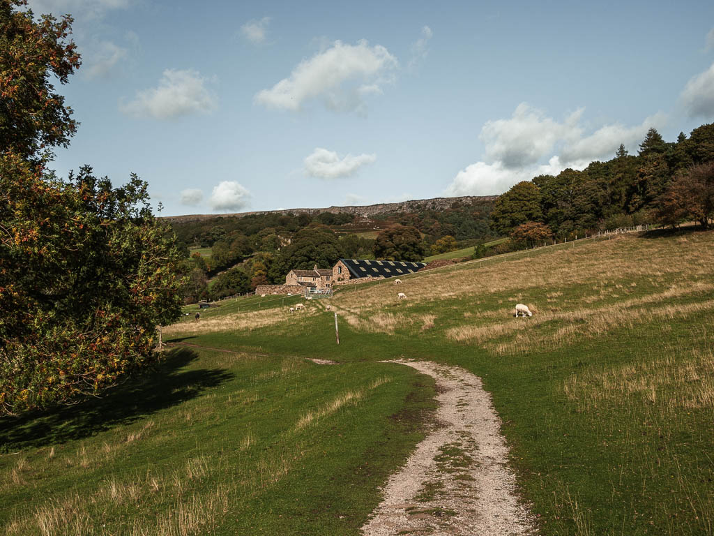 A trail cutting along the side of the hill, with a farmhouse building ahead. 