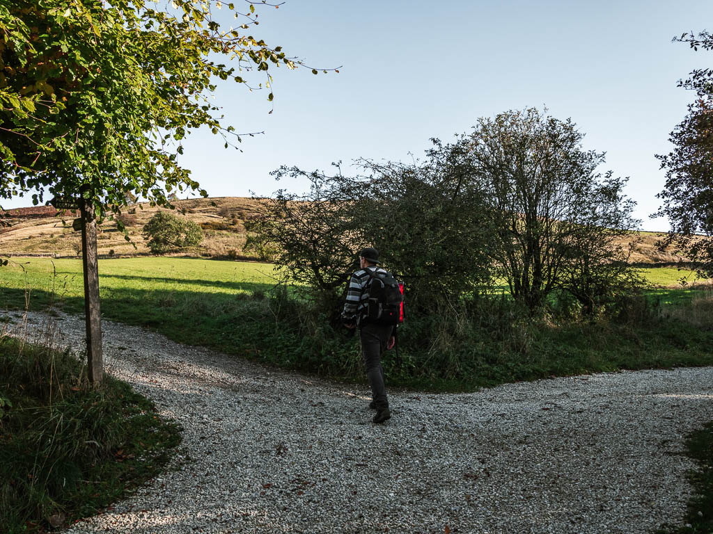 A gravel path trail split, with a man walking along the left trail.