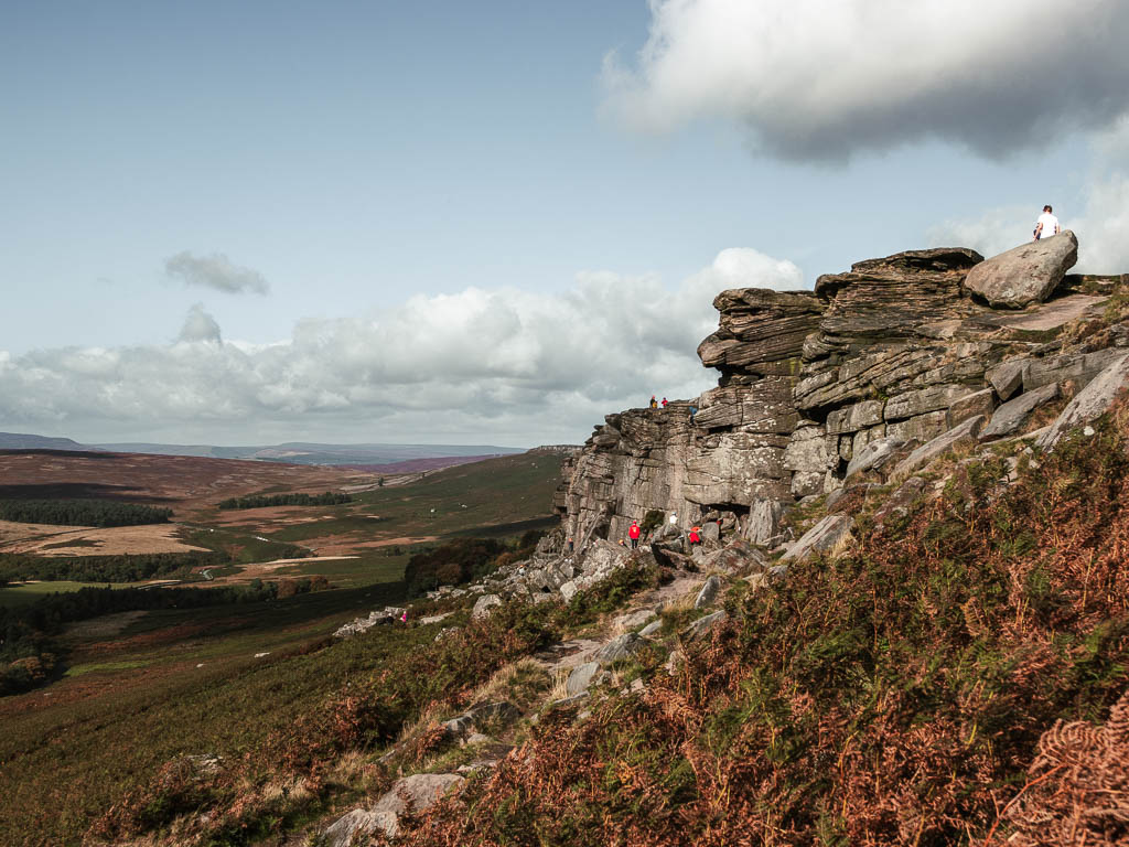 Looking along the side of the rock face of Stanage Edge, on the walk up to the top. There are rock climbers at the bottom. 