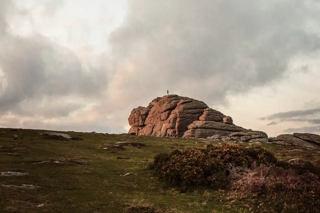 A person standing on top of a large tor, on a wild camping trip to Dartmoor National Park.