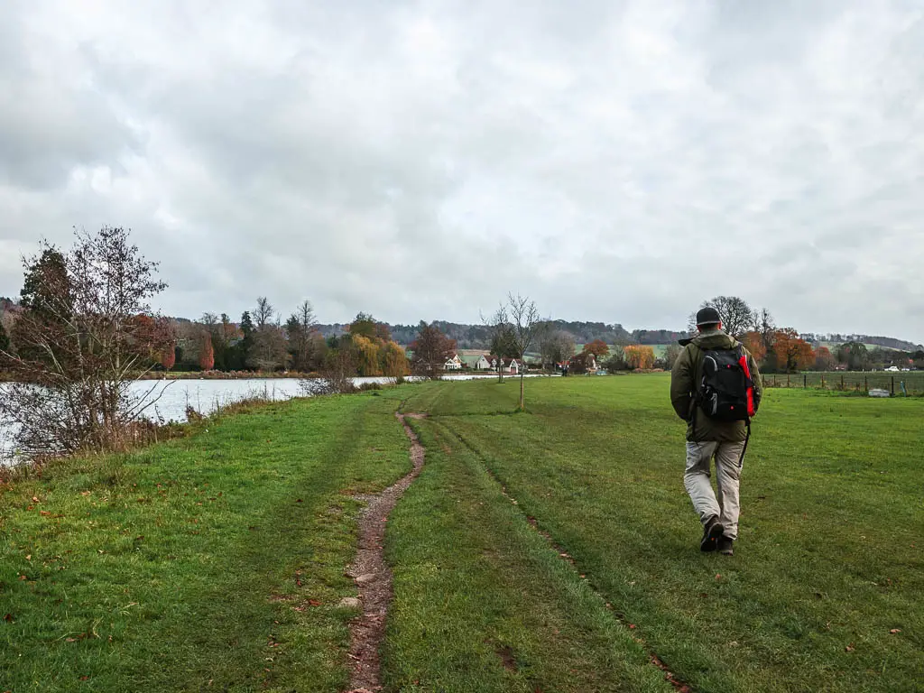 A narrow dirt trail through the neatly cut grass, with a man walking to the right of it, along the route from Henley to Hambleden.