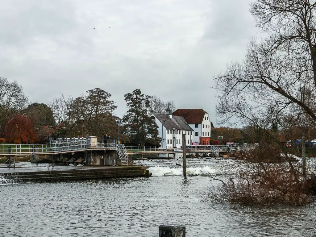 Looking across the river towards the gushing water of the weir, and some white coloured houses on thew other wide, on the walk to Hambleden from Henley.