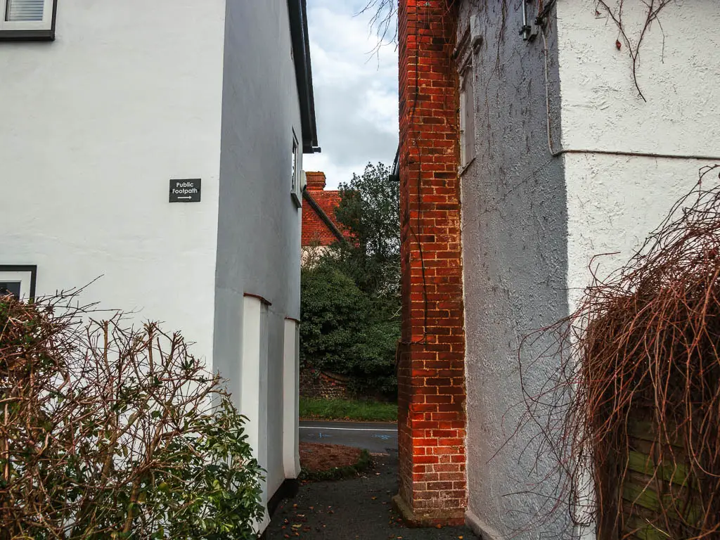A gap between the houses which are painted white, with a footpath sign on the wall of the left house.