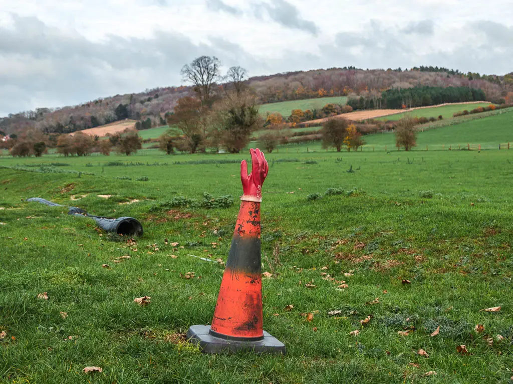 A red traffic cone with a red glove stuck on the top of it, in a large field.