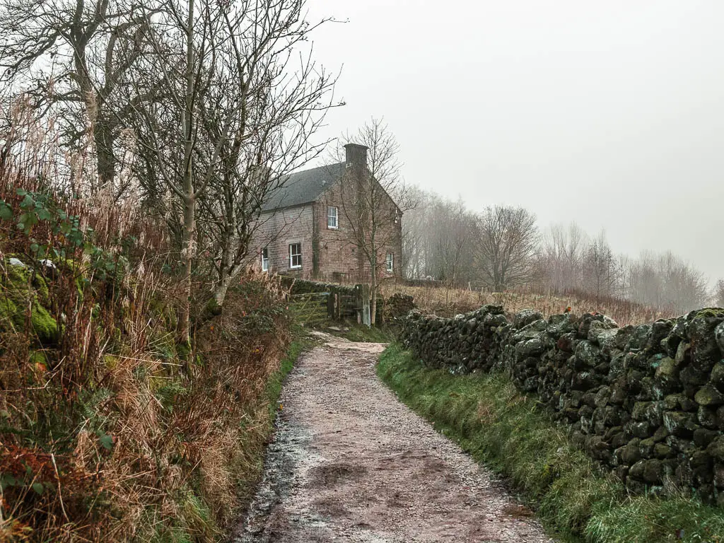 A path leading straight then curving right, on the walk towards Lud's Church. There is a stone wall to the right, and a house up ahead.