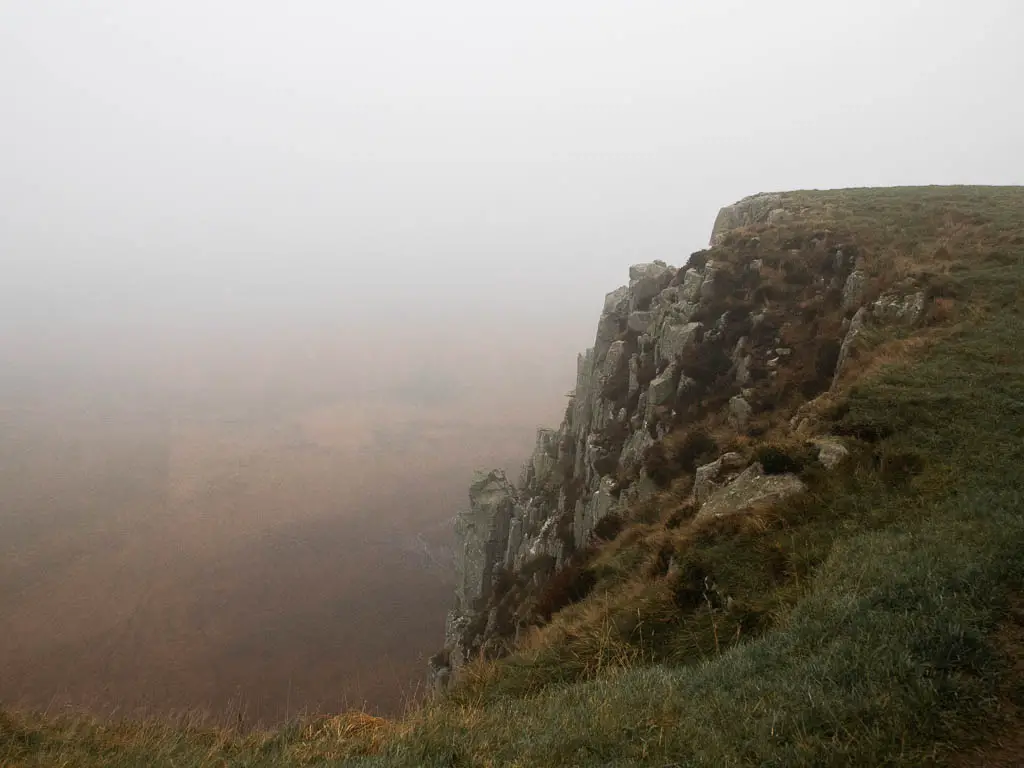 Looking down the side of a rocky cliff face, surround by fog.