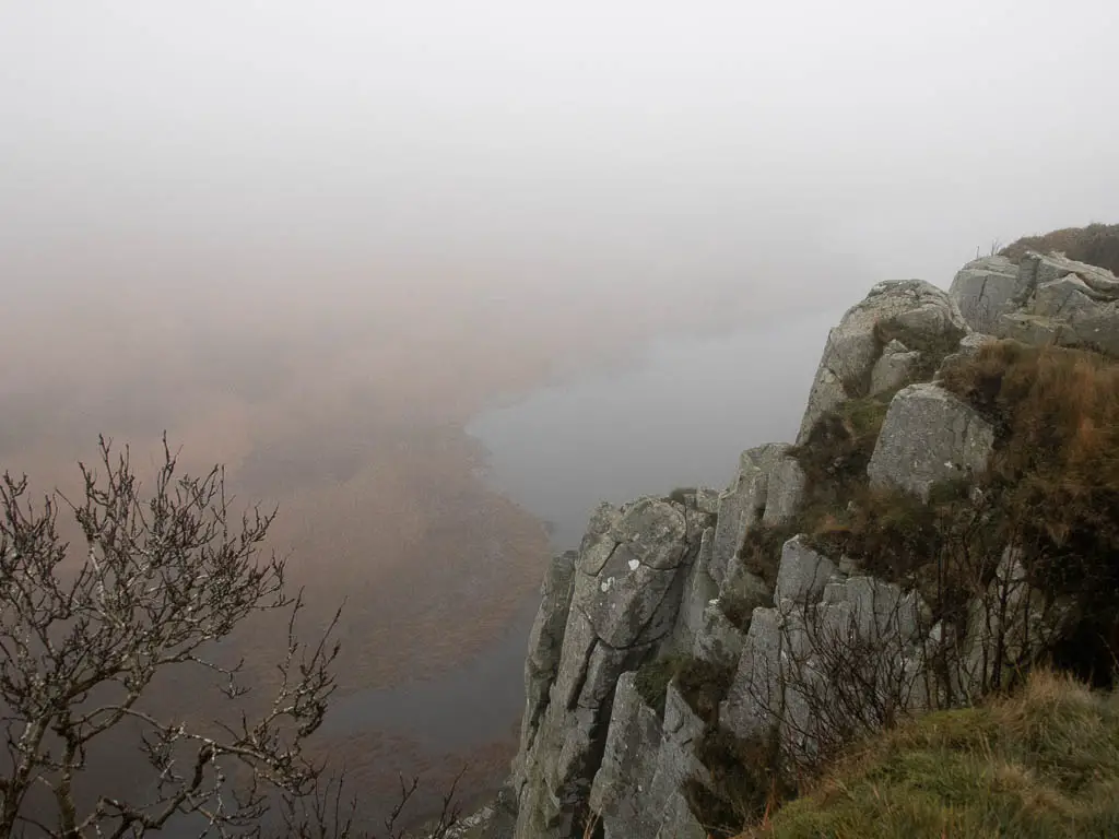 Looking down the side of a rock cliff on the Sycamore Gap walk. Crag Lough just about visible through the fog.