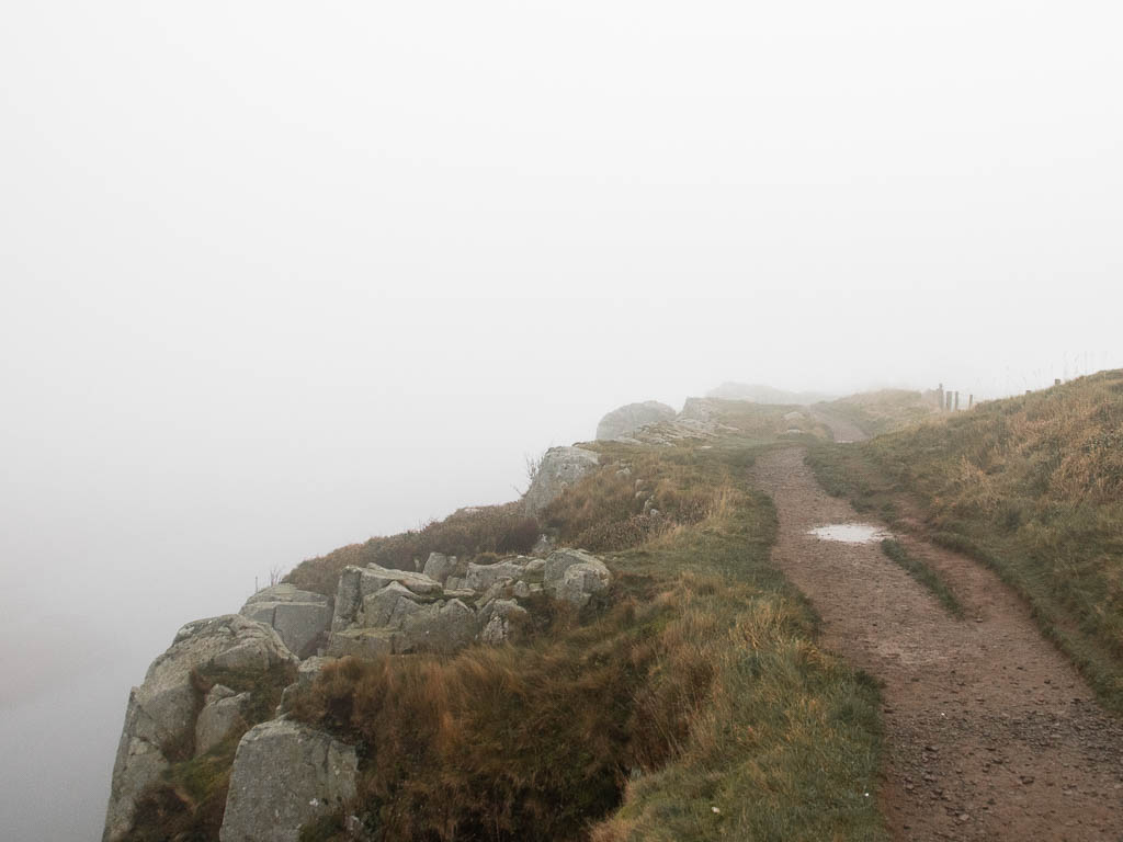 A dirt trail near the edge of a cliff on a foggy day, on the walk away from Sycamore Gap.