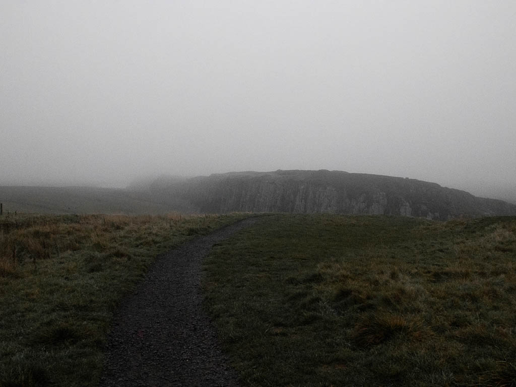 A gravel trail running through the grass, with a cliff visible ahead.