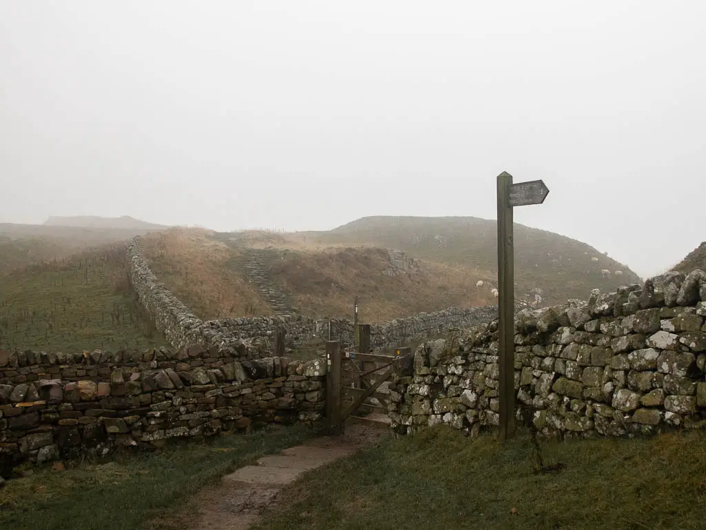 A junction of stone walls, with a gate and wooden trail signpost.