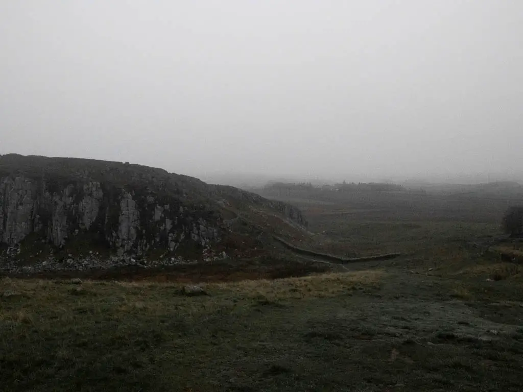 Looking across the grass towards a big hill, on a dark foggy day.