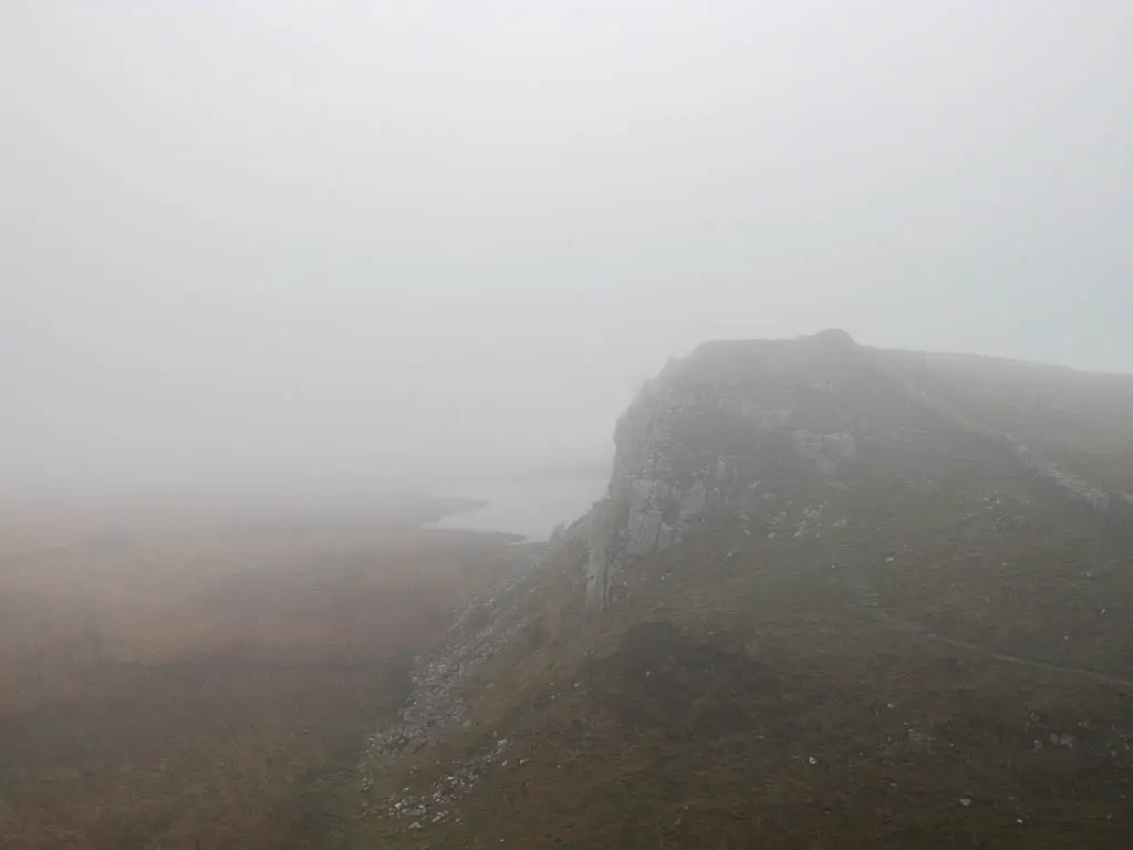 Its a foggy day, with the cliff side and Crag Lough just visible ahead, near the start of the Sycamore Gap walk.