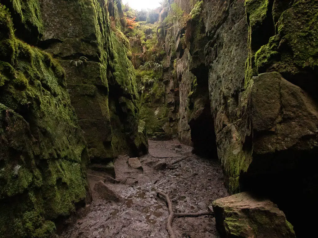 A muddy ground within a narrow passage enclosed by stone walls.