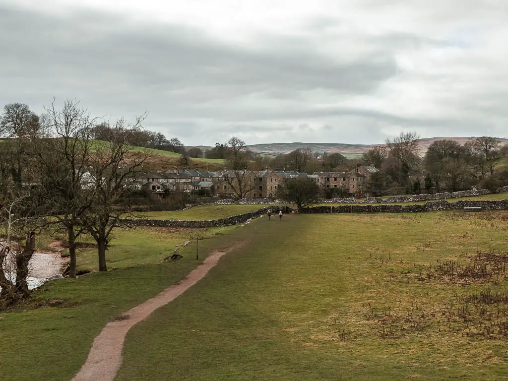 A path leading down and across the grass field towards a stone wall on the other side, and stone houses of Linton on the other side.