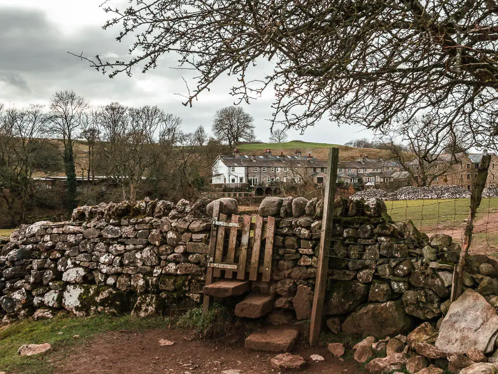 A small wooden gate in a stone wall, with a row of stone hoses visible ahead in the distance. 