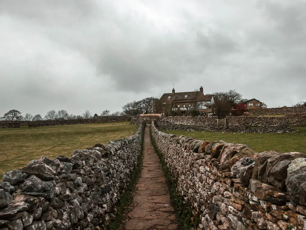 A narrow stone paved path lined with stone walls leading towards a budding in the other end on the walk into Grassington from the Linton Falls and Burnsall.