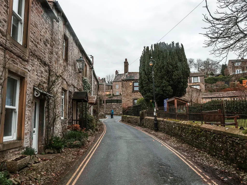 A road leading uphill, with stone walled houses on the left side and ahead.