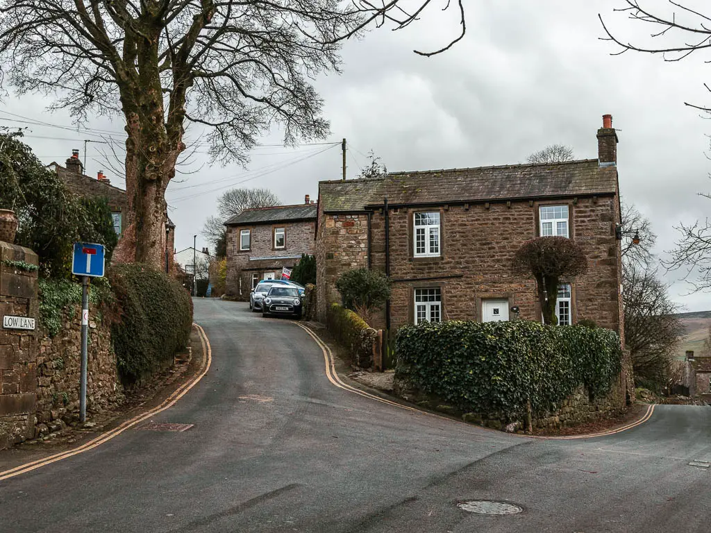 A road fork with a stone house in the junction. The left road leads uphill, and the road sign says 'Low Lane'.