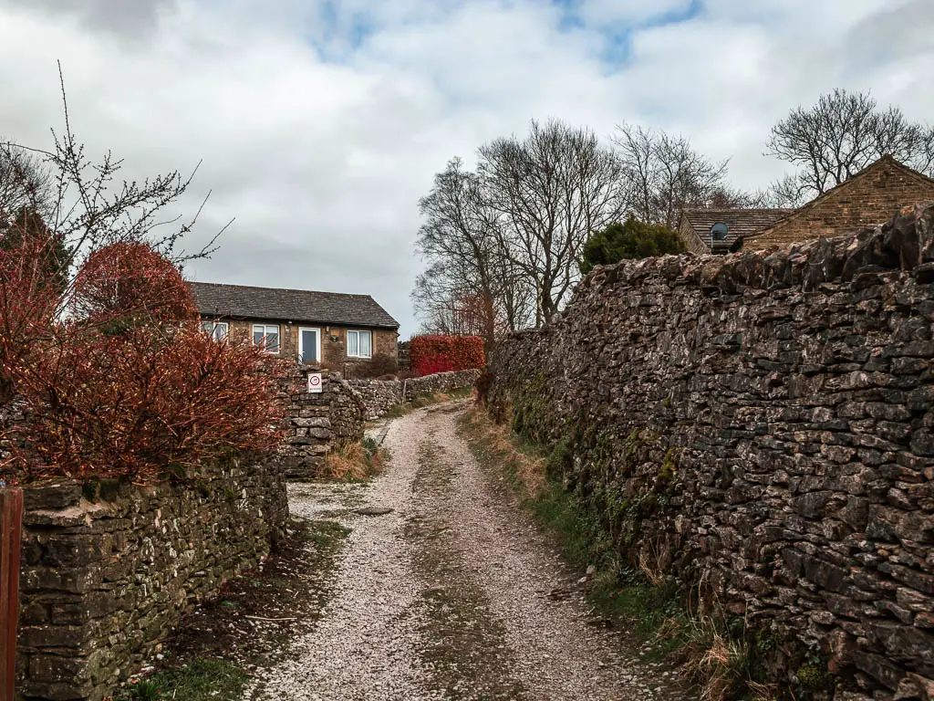 A gravel path leading uphill, lined with stone walls and a house ahead on the other side of the stone wall on the walk out of Grassington towards Burnsall.