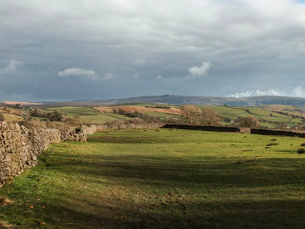 Looking down across a large grass field, surrounded by a stone wall on the walk back to Burnsall from Grassington. The sky is dark.