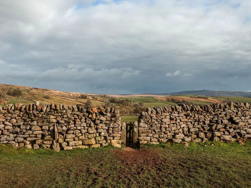 Small wooden gate in the stone wall on the circular walk back to Burnsall from Grassington. The sky is dark.