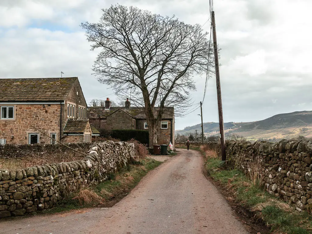 A road lined with stone walls and some stone buildings on the left.