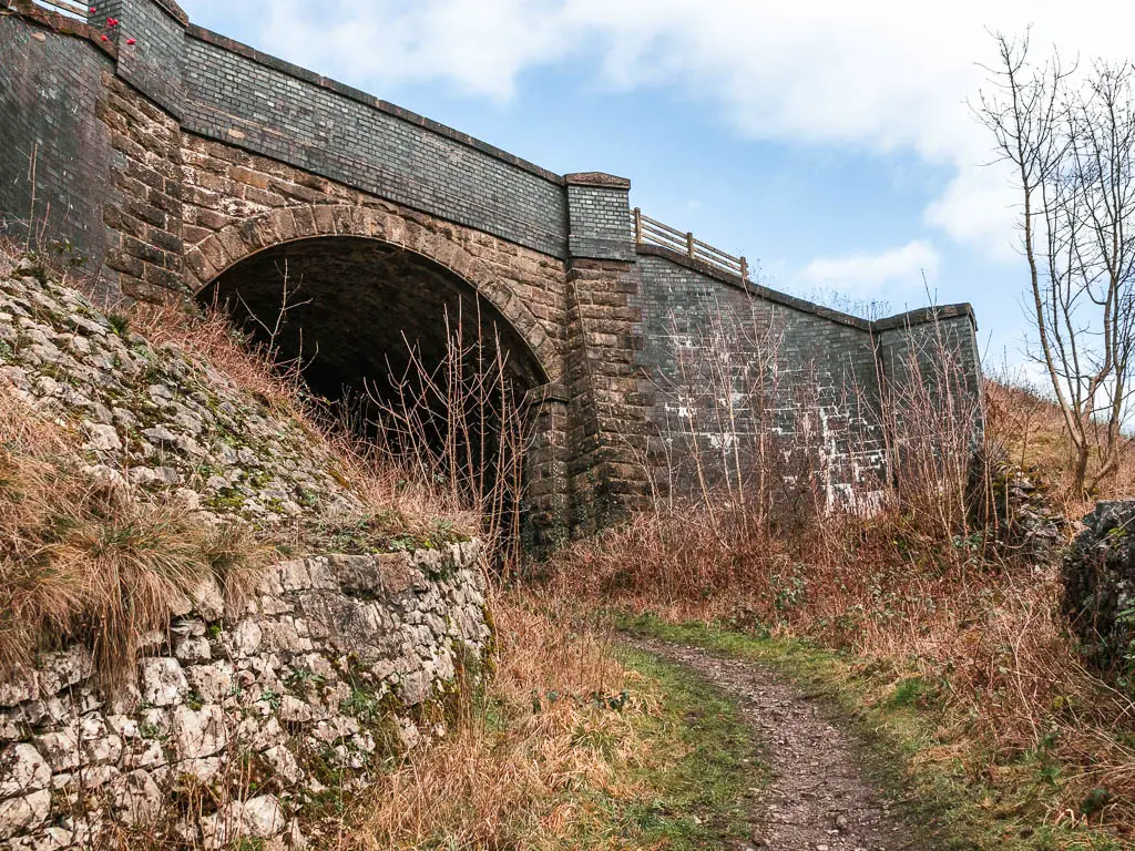 A dirt trail leading up and under an archway of a bridge.